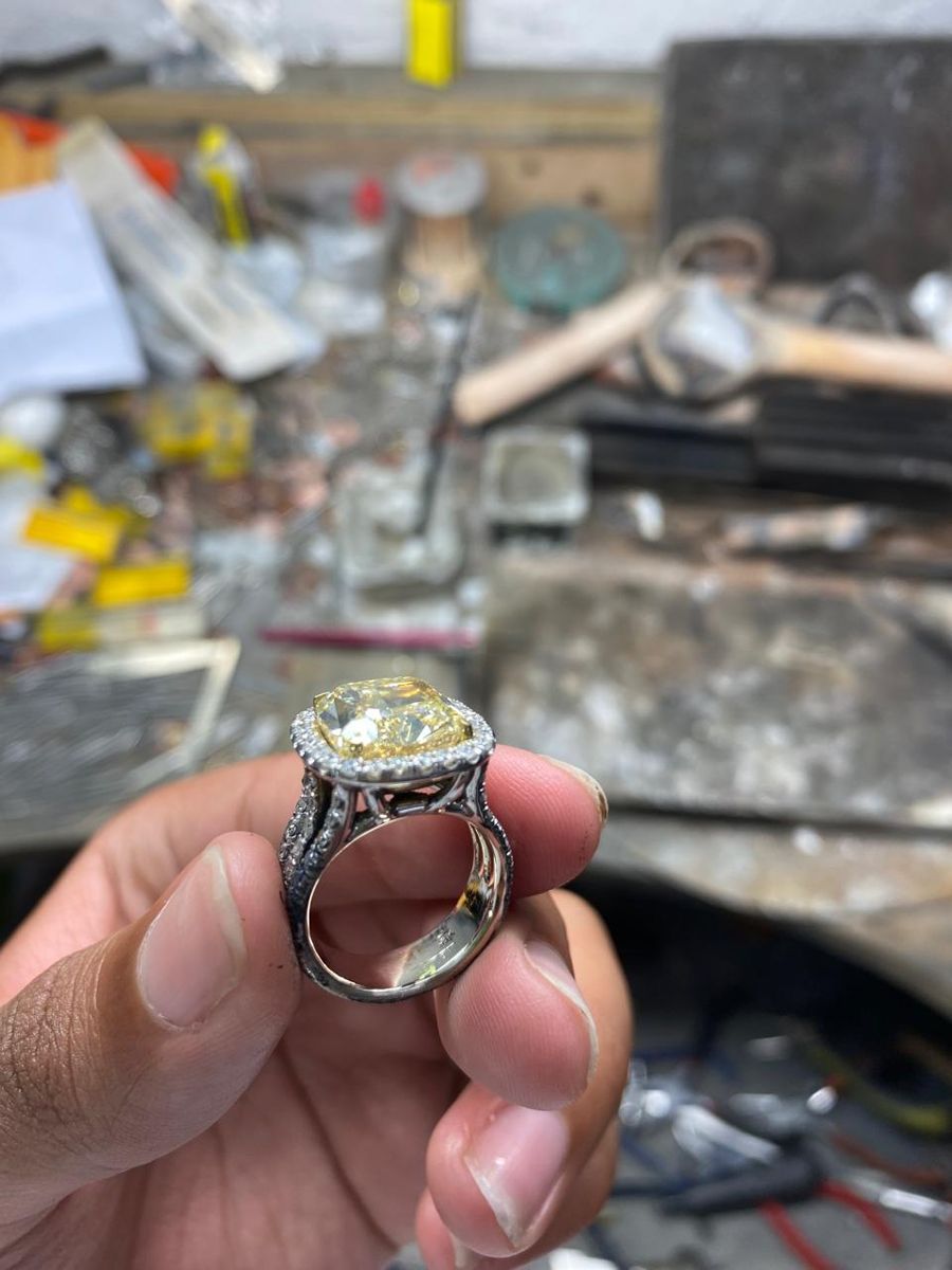 A yellow diamond ring with a diamond halo, held over the jeweler's workbench